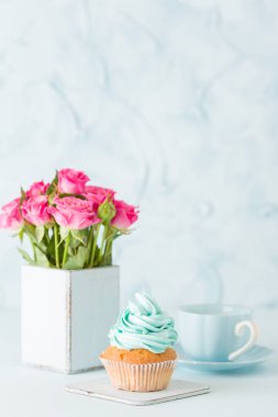 Cupcake pastel mavi zemin üzerine retro eski püskü şık vazoda nazik mavi krem ve pembe Gül ile.
