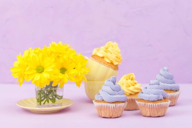 Sarı ve mor krem ve Kasımpatı Menekşe pastel arka planda tebrik kartı copyscape ile süslenmiş cupcakes.