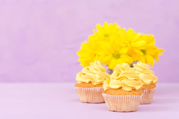 Cupcakes decorados com creme amarelo e crisântemos em fundo pastel violeta para cartão de saudação com copyscape . — Fotografia de Stock
