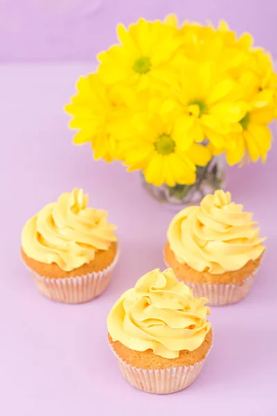 Babeczki, zdobione żółty krem i chryzantemy na fioletowe pastelowe tło dla karty z pozdrowieniami z copyscape. — Zdjęcie stockowe