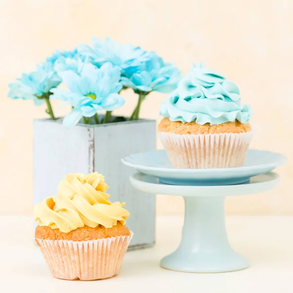 Cupcake with sweet blue and yellow buttercream decoration and blue chrysanthemum in retro shabby chic vase.