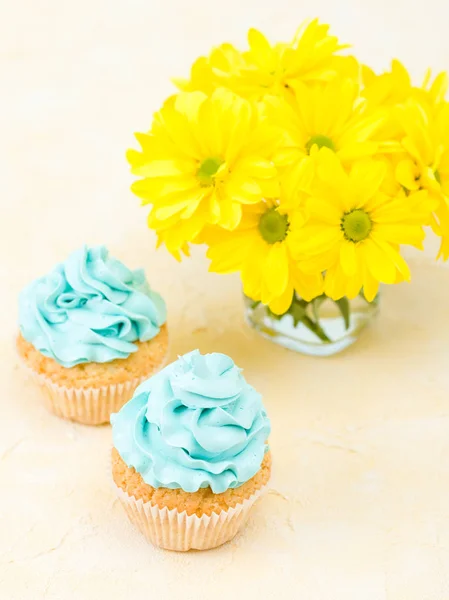 Cupcake com concurso azul creme decoração e buquê de crisântemo amarelo em vidro sobre fundo pastel . — Fotografia de Stock