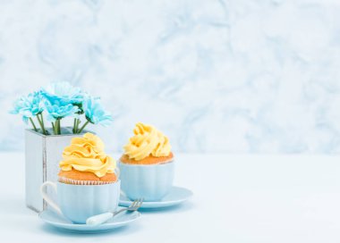Cupcake ihale sarı krem dekorasyon ve retro eski püskü şık vazoda pastel mavi zemin üzerine mavi papatya buketi ile.