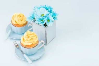 Cupcake ihale sarı krem dekorasyon ve retro eski püskü şık vazoda pastel mavi zemin üzerine mavi papatya buketi ile.