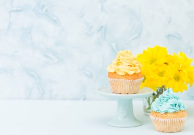 Tatlı sarı krem dekorasyon ve pastel mavi zemin üzerine retro eski püskü şık vazoda sarı Kasımpatı buket cupcake.