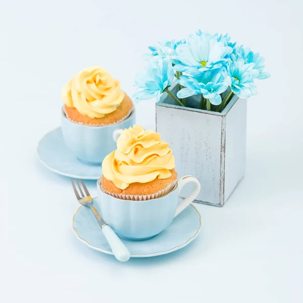 Cupcake con tierna decoración de crema amarilla y ramo de crisantemo azul en jarrón retro shabby chic sobre fondo pastel azul . — Foto de Stock