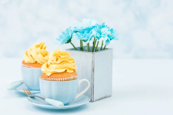 Cupcake mit zarter gelber Cremedekoration und einem Strauß blauer Chrysanthemen in Retro-Shabby-Chic-Vase auf blauem Pastell-Hintergrund. — Stockfoto
