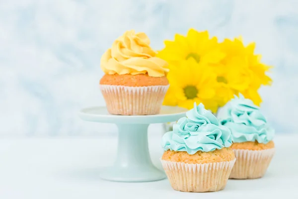 Cupcake com doce decoração creme amarelo e buquê de crisântemo amarelo em vaso chique retro gasto em fundo pastel azul . — Fotografia de Stock