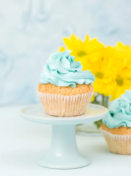 Cupcake com decoração creme azul no estande vintage e buquê de crisântemo amarelo em vaso de óculos . — Fotografia de Stock