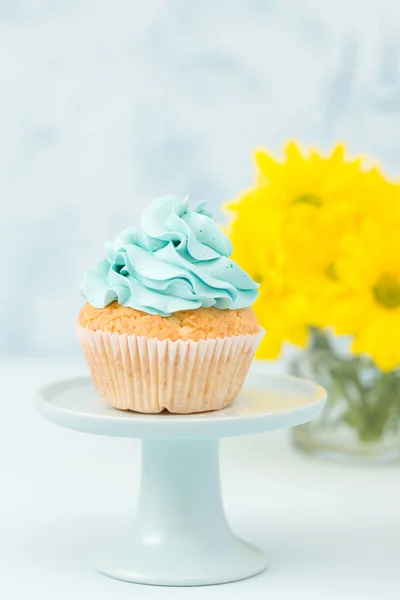 Cupcake with blue cream decoration on vintage stand and bouquet of yellow chrysanthemum in glasses vase.