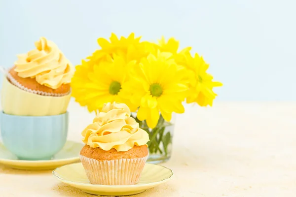 Cupcake with yellow cream decoration and bouquet of yellow chrysanthemum in small glass.