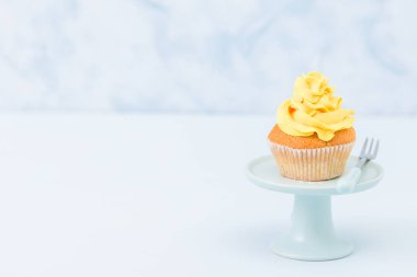 Cupcake vintage üzerinde sarı krem dekorasyonu ile mavi pastel arka plan üzerinde durmak. Gıda minimalist kavramı.