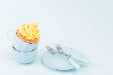 Pastel mavi zemin üzerine iki küçük bardak tatlı sarı krem süslemeli cupcake.