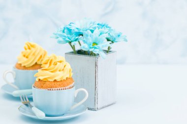 Cupcake ihale sarı krem dekorasyon ve retro eski püskü şık vazoda pastel mavi zemin üzerine mavi papatya buketi ile.