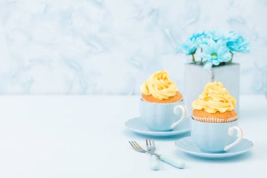 Cupcake ihale sarı krem dekorasyon ve retro eski püskü şık vazoda pastel mavi zemin üzerine mavi papatya buketi ile.