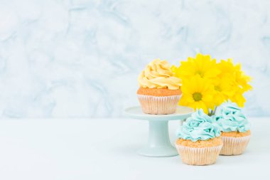 Tatlı sarı krem dekorasyon ve pastel mavi zemin üzerine retro eski püskü şık vazoda sarı Kasımpatı buket cupcake.