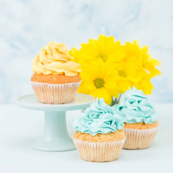 Cupcake com doce decoração creme amarelo e buquê de crisântemo amarelo em vaso chique retro gasto em fundo pastel azul . — Fotografia de Stock