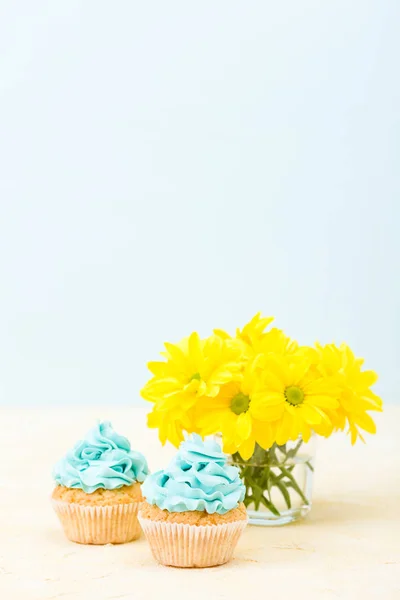 Cupcake with blue cream decoration and bouquet of yellow chrysanthemum. Copycpase concept