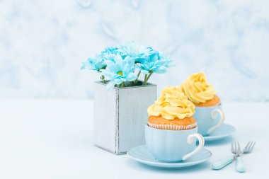 İhale sarı krem dekorasyon ve retro eski püskü şık vazoda pastel mavi zemin üzerine mavi krizantem buket ile cupcakes.