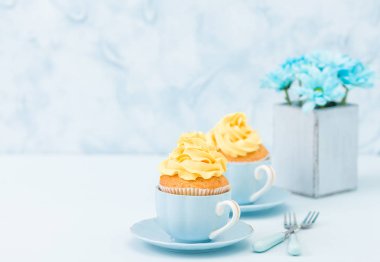Cupcake ihale sarı krem dekorasyon ve retro eski püskü şık vazoda pastel mavi zemin üzerine mavi papatya buketi ile.