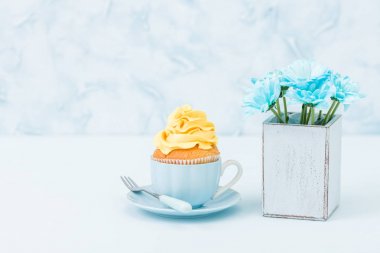 Cupcake ihale sarı krem dekorasyon ve retro eski püskü şık vazoda pastel mavi zemin üzerine mavi papatya buketi ile.