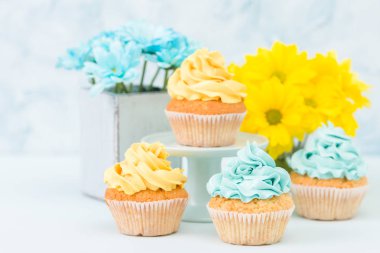 Sarı ve mavi krem dekorasyon ve Kasımpatı pastel arka plan üzerinde retro eski püskü şık vazoda demetleri ile cupcakes.
