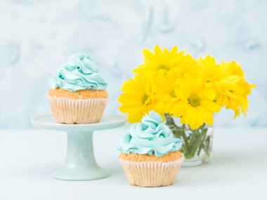 Mavi krem dekorasyon stand ve pastel mavi zemin üzerine gözlük vazoda sarı Kasımpatı buket ile cupcakes.