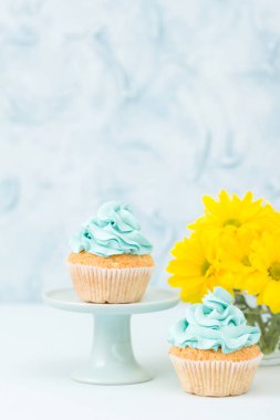 Mavi krem dekorasyon stand ve pastel mavi zemin üzerine gözlük vazoda sarı Kasımpatı buket ile cupcakes.