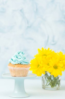 Cupcake standı ve pastel mavi zemin üzerine cam vazoda sarı Kasımpatı buket mavi krem dekorasyonu ile.