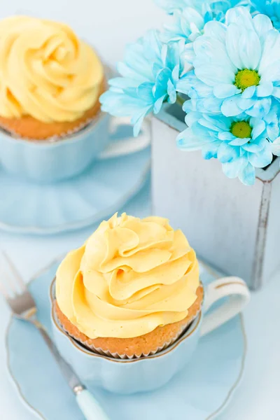 Cupcakes con tierna decoración de crema amarilla y ramo de crisantemo azul en jarrón retro shabby chic sobre fondo pastel azul . — Foto de Stock