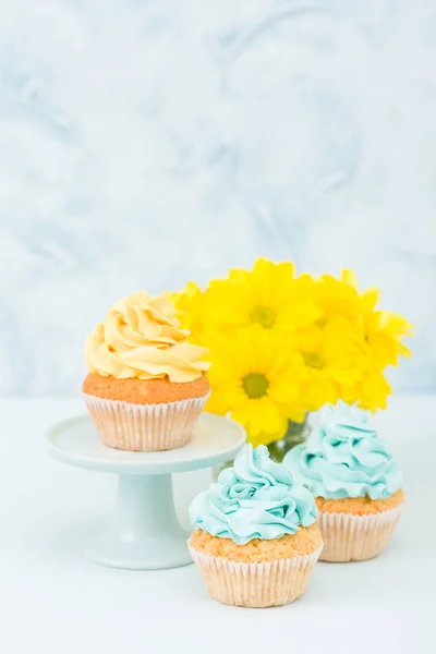 Cupcakes com decoração de creme amarelo e azul e buquê de crisântemo amarelo no fundo pastel . — Fotografia de Stock