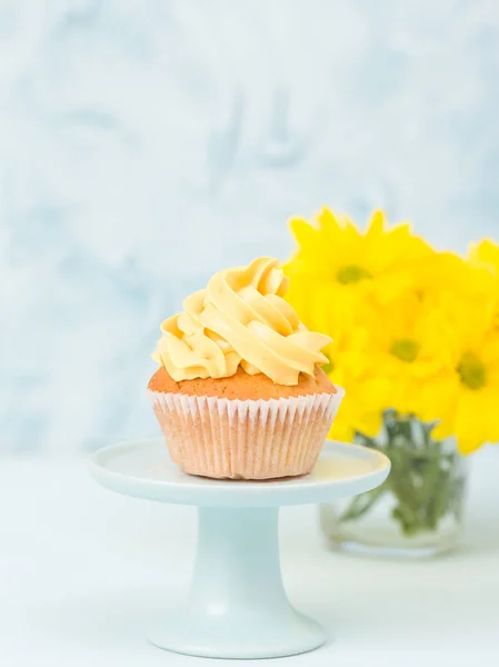 Ciastko z żółty krem dekoracja na stoisko i bukiet Chryzantema w szklanym wazonie na niebieskim tle pastel. — Zdjęcie stockowe