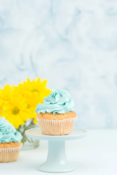 Cupcake com decoração creme azul no estande vintage e buquê de crisântemo amarelo em vaso de óculos . — Fotografia de Stock