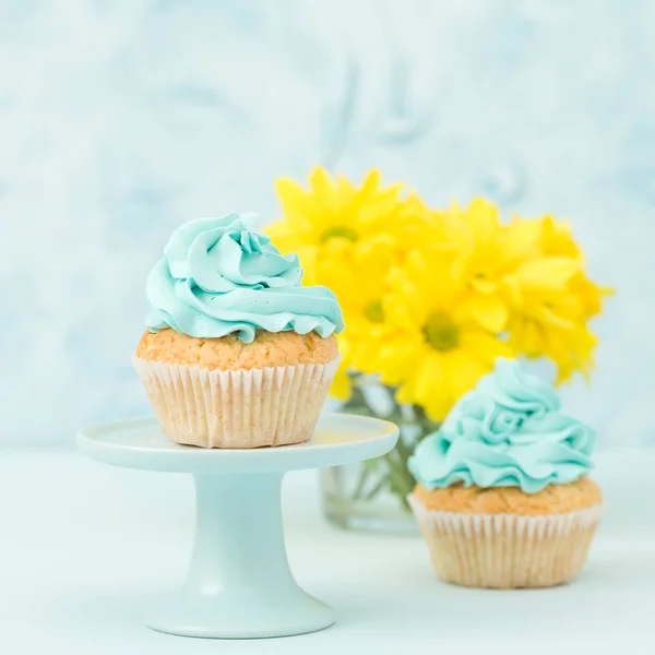 Cupcake mit Dekoration aus blauer Sahne auf Vintage-Ständer und Bouquet aus gelben Chrysanthemen in Glasvase. — Stockfoto