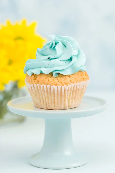 Cupcake com decoração creme azul no estande vintage e buquê de crisântemo amarelo em vaso de óculos . — Fotografia de Stock