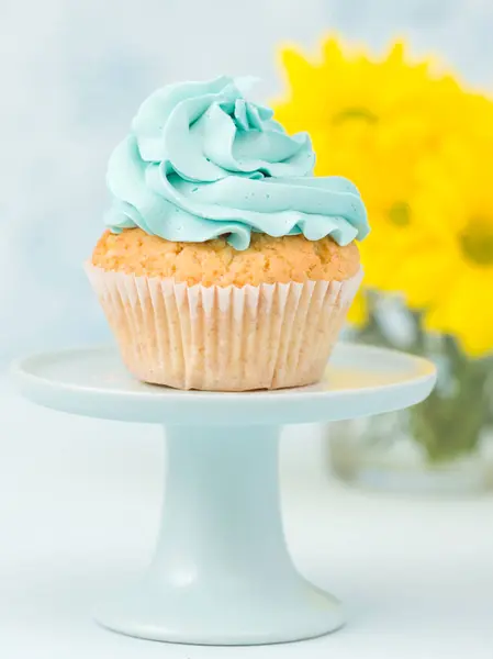 Cupcake com decoração creme azul no estande vintage e buquê de crisântemo amarelo em vaso de óculos . — Fotografia de Stock