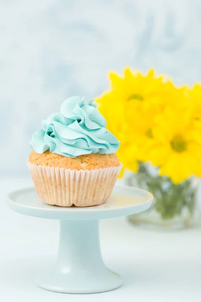 Cupcake com decoração creme azul no estande vintage e buquê de crisântemo amarelo em vaso de óculos . — Fotografia de Stock