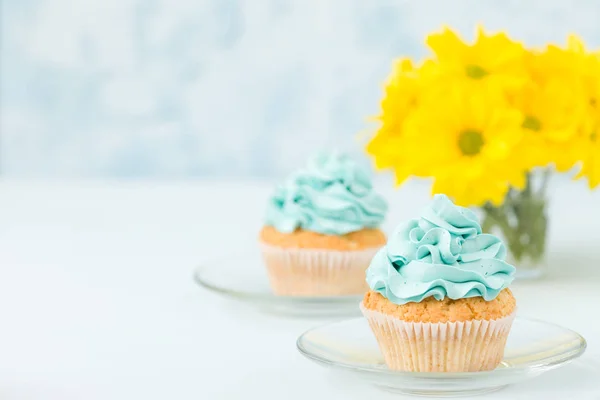 Cupcake com doce decoração creme azul em sauser e buquê de crisântemo amarelo em copos copo . — Fotografia de Stock