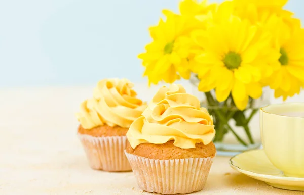Cupcake with yellow cream decoration, coffee with milk and bouquet of yellow chrysanthemum in small glasses cup.