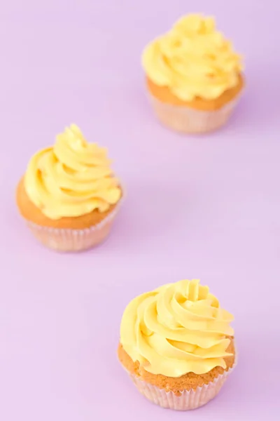 紫色のパステル調の背景に黄色のクリームと飾られるカップケーキ. — ストック写真