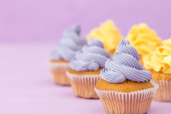 Cupcakes decorados con decoraciones de crema amarilla y violeta sobre fondo pastel . — Foto de Stock