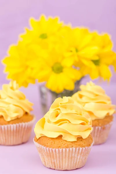 Cupcakes decorados com creme amarelo e crisântemos em fundo pastel violeta . — Fotografia de Stock