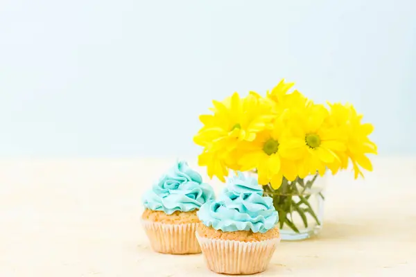 Cupcakes com decoração de creme azul e buquê de crisântemo amarelo em vidro sobre fundo pastel . — Fotografia de Stock