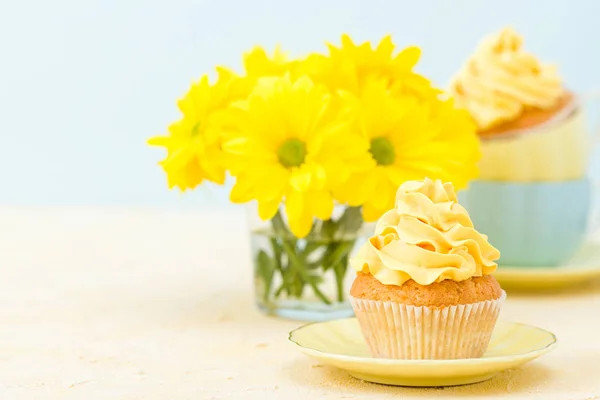 Cupcake com decoração de creme amarelo e buquê de crisântemo amarelo em vidro sobre fundo pastel concurso . — Fotografia de Stock