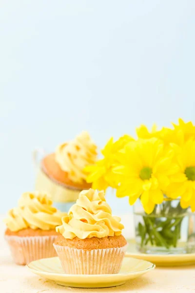 Cupcake with yellow cream decoration and bouquet of yellow chrysanthemum in glass on tender pastel background. — Stock Photo, Image