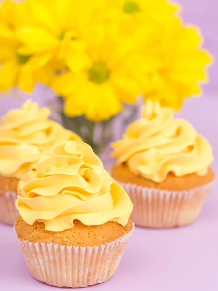 Cupcakes decorated with yellow cream and chrysanthemums on violet pastel background.