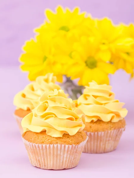 Babeczki zdobione żółty krem i chryzantemy na fioletowym tle pastel. — Zdjęcie stockowe