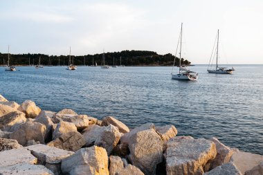 Gün batımında taş iskele. Bir direk ve yelken ile deniz yelkenli tekne. Bir ada fonunda
