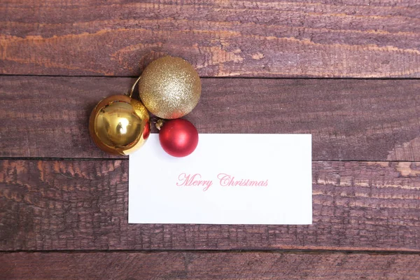 Text Frohe Weihnachten auf Papier mit Kugeln über Holzgrund — Stockfoto