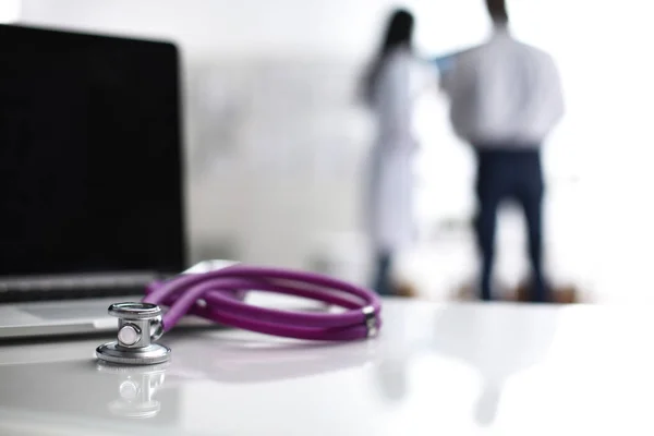 Laptop and stethoscope on the desk , doctors standing in the background — Stock Photo, Image